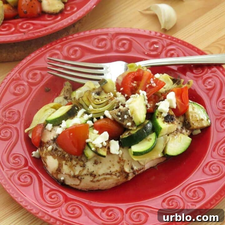 A serving of Mediterranean chicken bake with zucchini, artichokes, tomatoes, and a balsamic vinaigrette on a plate with a fork.