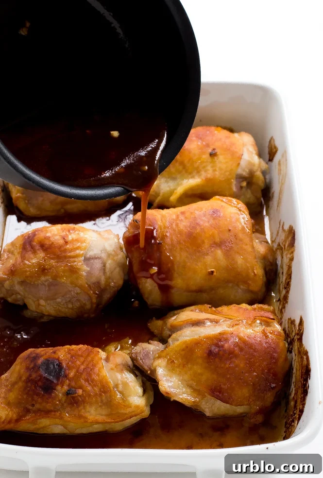 Baked Honey Garlic Chicken Thighs in a white baking dish being topped with the honey garlic sauce 