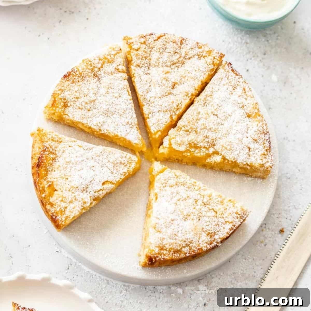 Overhead shot of Lemon Curd Cake, with a slice missing, sitting on a round white dish.