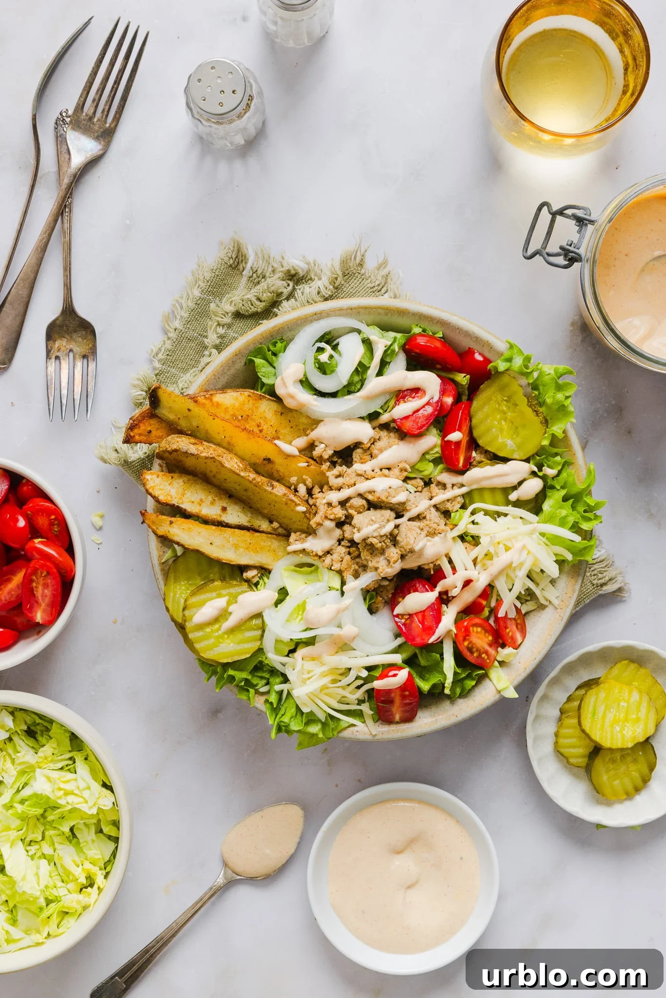 Loaded turkey burger bowl with potato wedges and veggies drizzled with burger sauce, additional veggies in small bowls on the side.