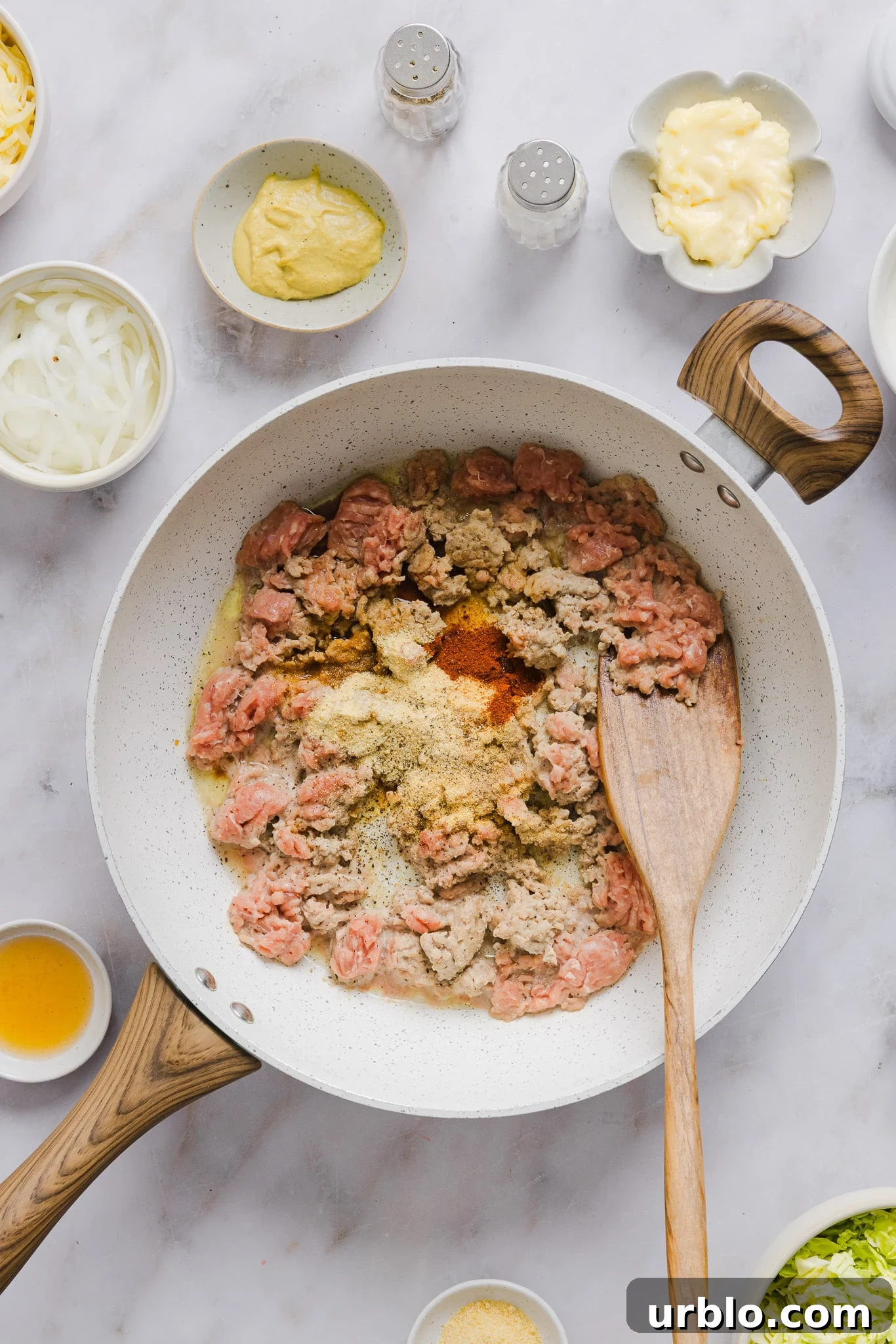 Ground turkey and seasonings in a frying pan with a wooden spoon.