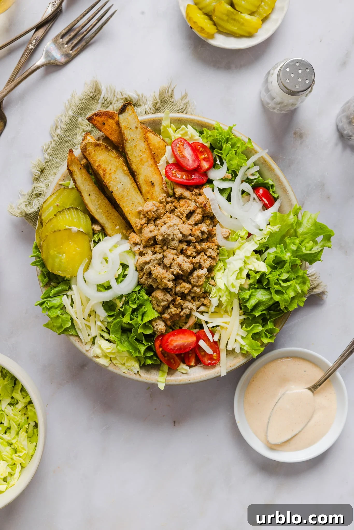 Turkey burger bowl topped with potato wedges, pickles, onions, lettuce, tomato with burger sauce on the side in a small dish.