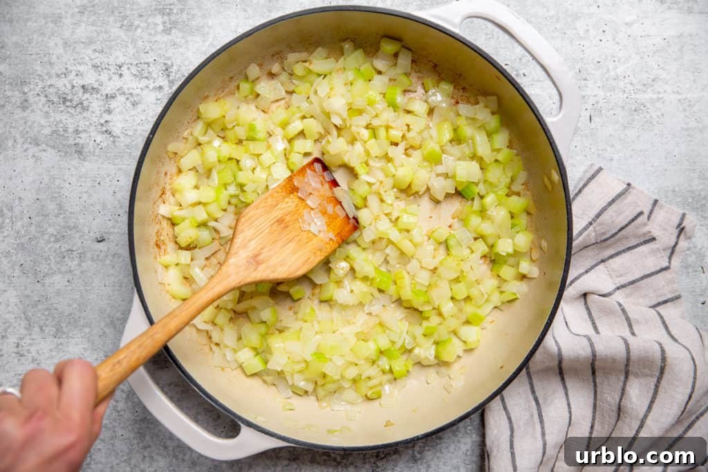 Gluten-Free Cornbread Stuffing Recipe (Cornbread Dressing) 6 Process shot showing a hand stirring cooked celery and onion in a large skillet.