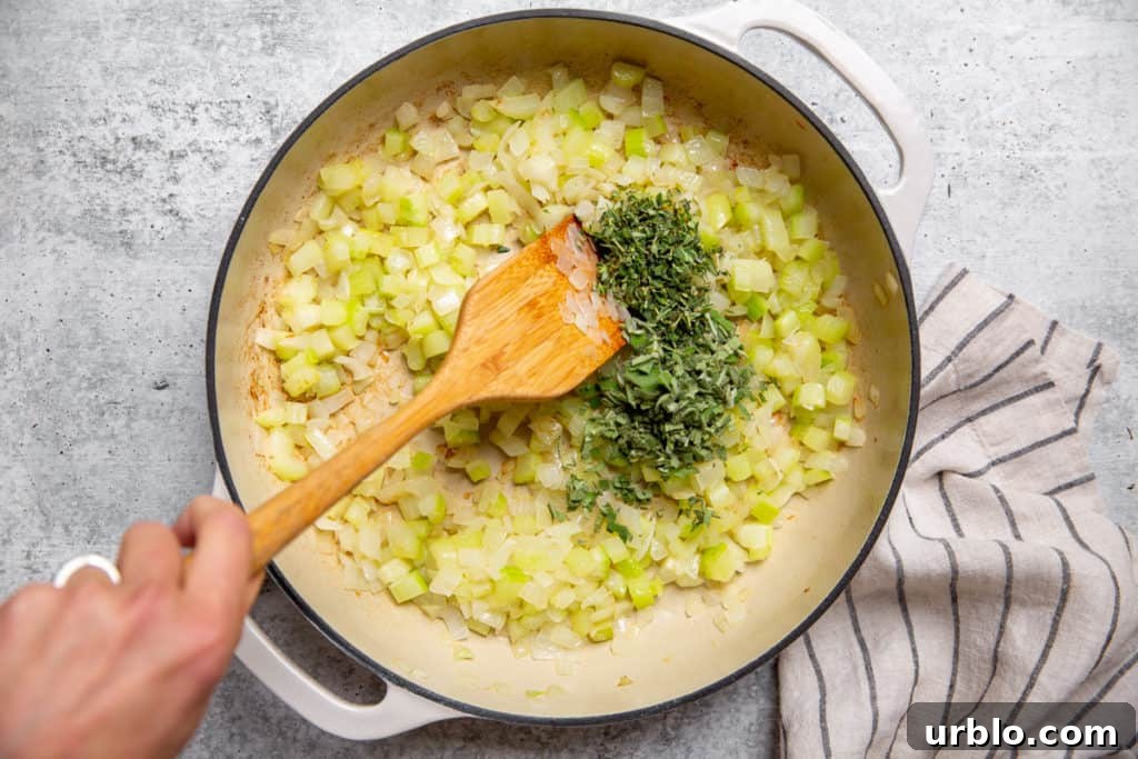 Gluten-Free Cornbread Stuffing Recipe (Cornbread Dressing) 7 Wooden spoon stirring chopped sage and thyme into a skillet with cooked onion and celery.