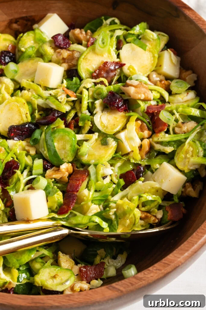 closeup of shaved brussel sprout salad in a wooden serving bowl with gold serving spoons.