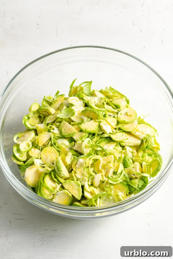 plain raw shaved brussels sprouts in a clear mixing bowl.