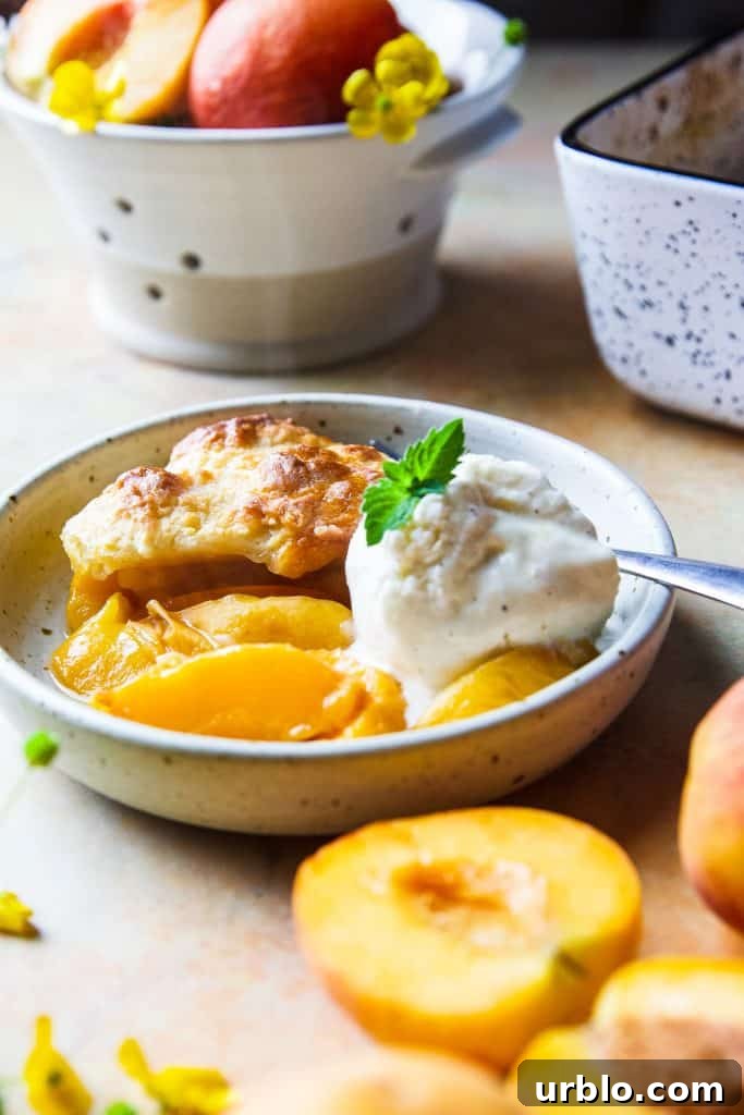 Slice of peach cobbler on a small plate with vanilla ice cream.