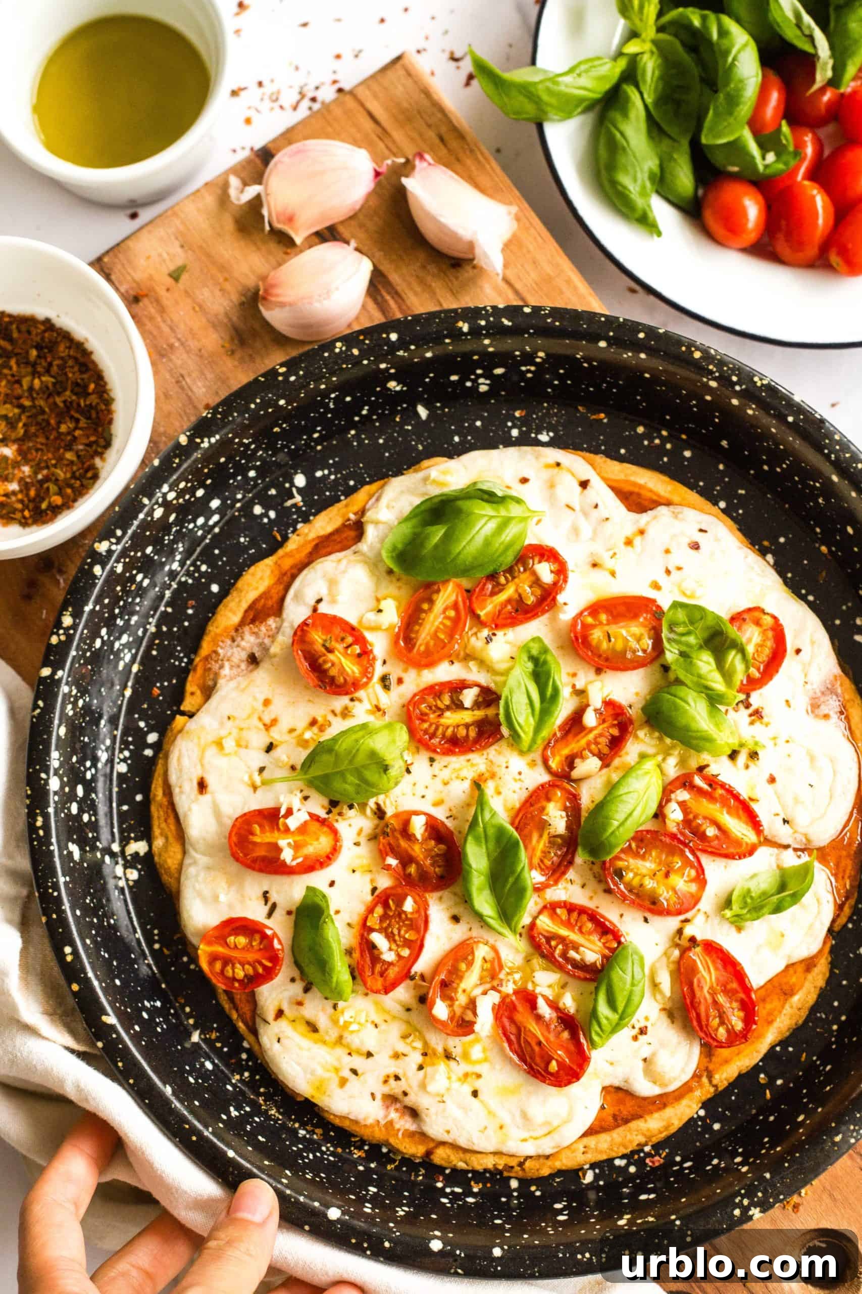 Hand holding a pizza pan with freshly baked gluten-free caprese pizza.