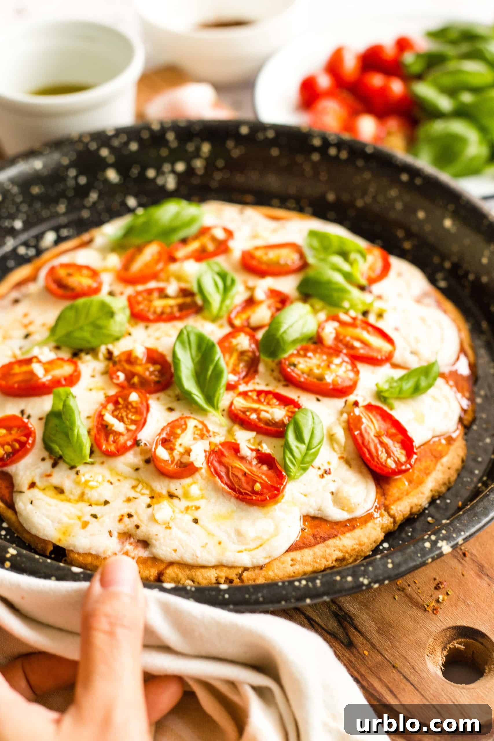 Hand holding a pizza pan with a freshly baked gluten-free caprese pizza.