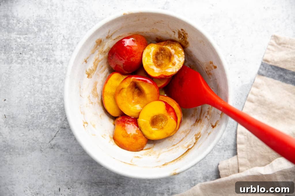 Process shot showing peach halves in a bowl with honey, cinnamon, cardamom and vanilla. 