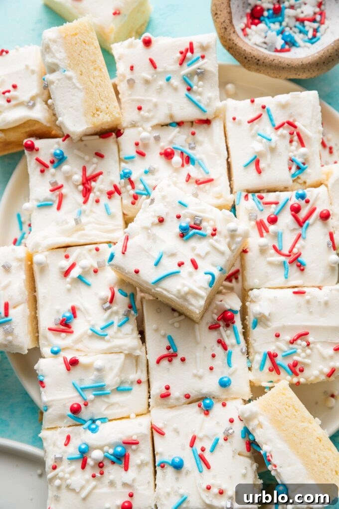 Patriotic Red, White & Blue Sugar Cookie Bars Recipe 3 Large pile of sugar cookie bars topped with white frosting and a red, white, and blue sprinkle mix.