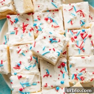 Patriotic Red, White & Blue Sugar Cookie Bars Recipe 4 Large pile of sugar cookie bars topped with white frosting and a red, white, and blue sprinkle mix.