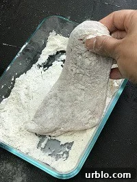 dredging chicken cutlet with flour in a glass rectangular container