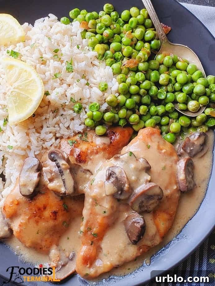chicken marsala served on a black plate with brown rice, green peas & lemon wedges