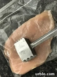 pounding chicken inside a zip lock bag with a metal pounder