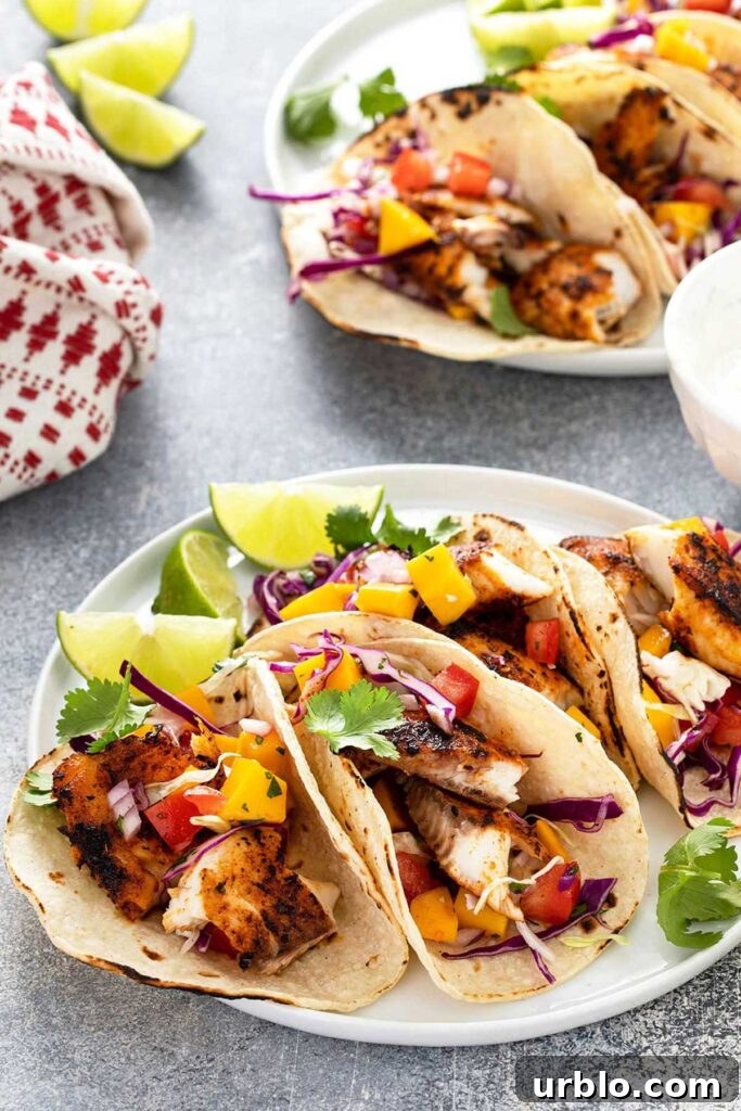 Four Blackened Fish Tacos with mango slaw on a white plate with slices of lime.