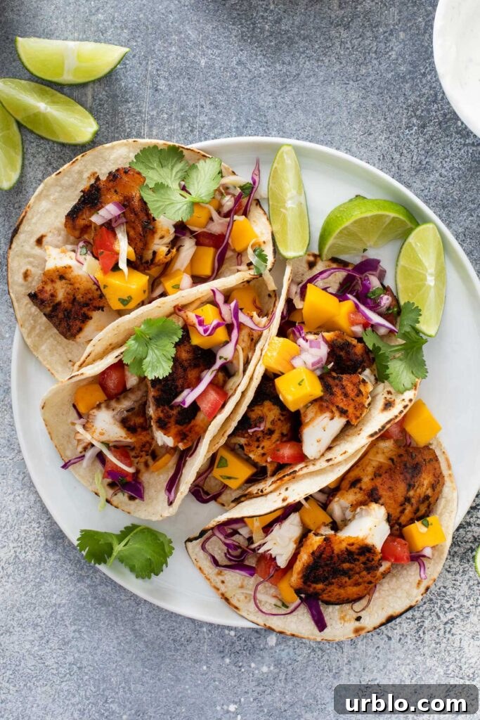 Top view of 4 Blackened Fish Tacos on a white plate with slices of lime.