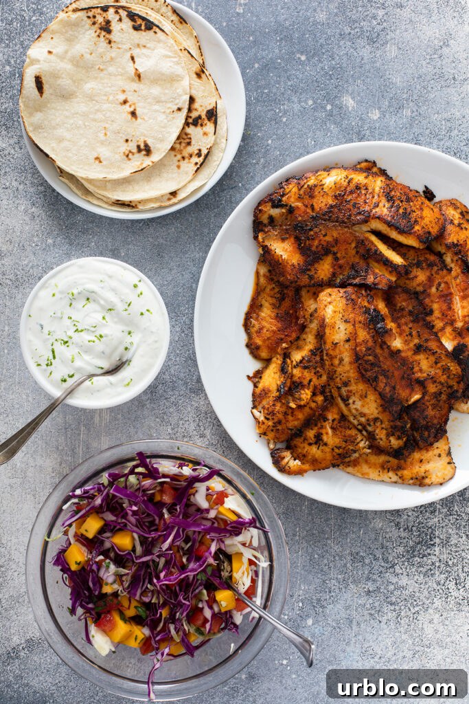 Cooked, blackened fish in a white plate ready to be served alongside a plate of corn tortillas, freshly made lime crema, and mango slaw