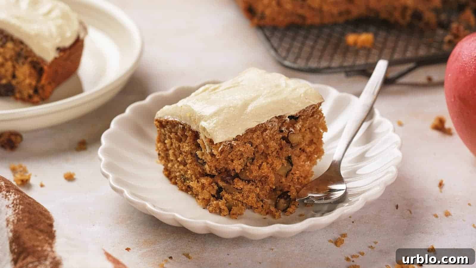 21 Crowd-Pleasing Potluck Recipes That Outshine Store-Bought Dishes 9 A slice of frosted applesauce cake with nuts on a white scalloped plate, accompanied by a fork.