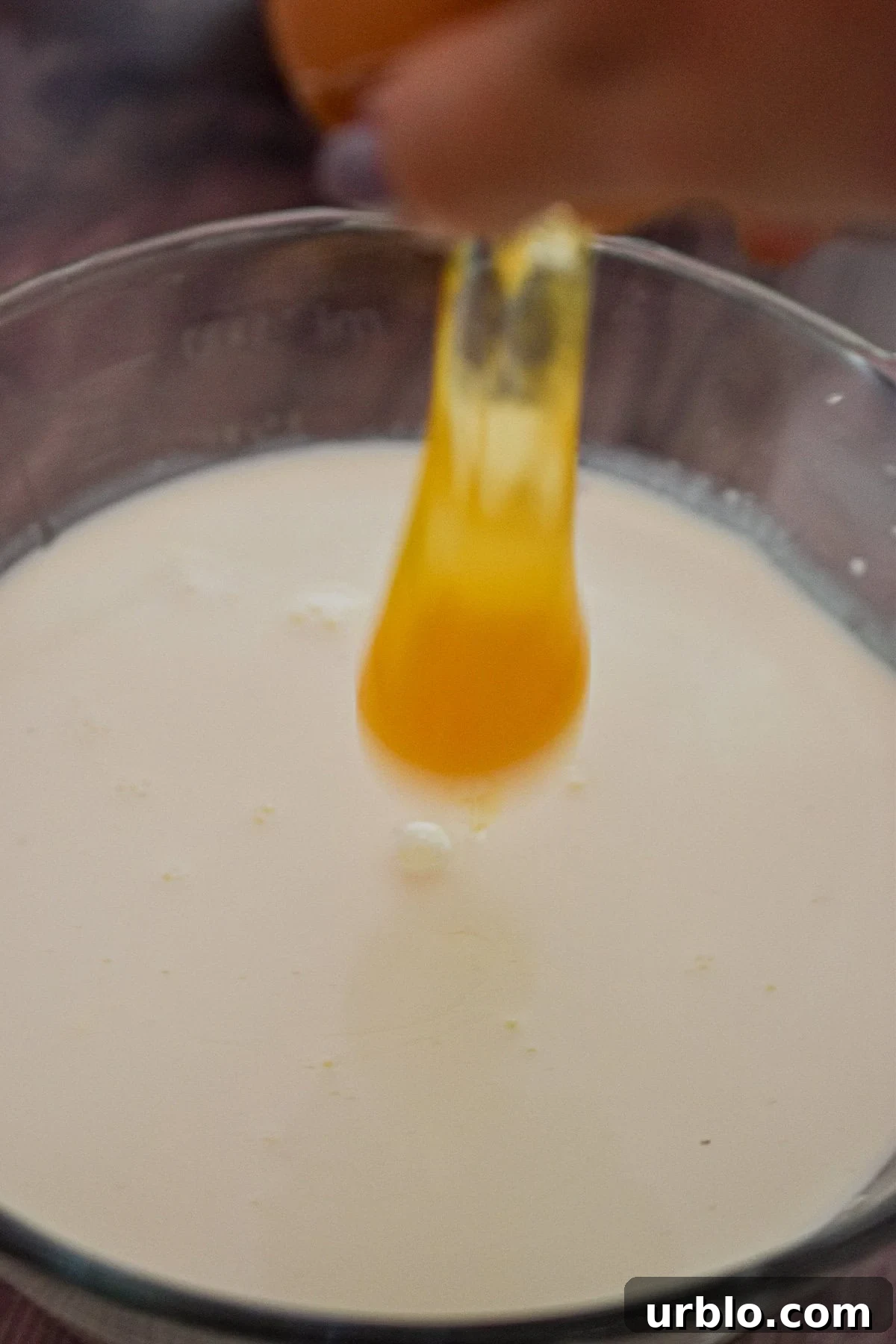 An egg is being cracked into a liquid measuring cup filled with milk.