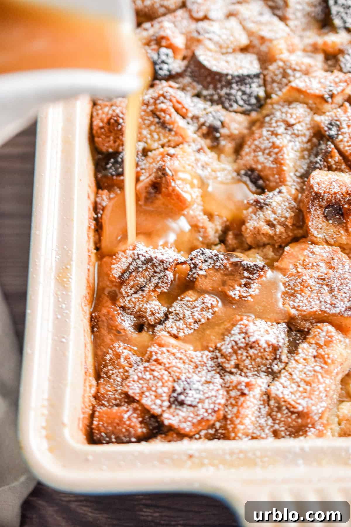 The caramel sauce is being poured over the pan full of the sourdough bread pudding.