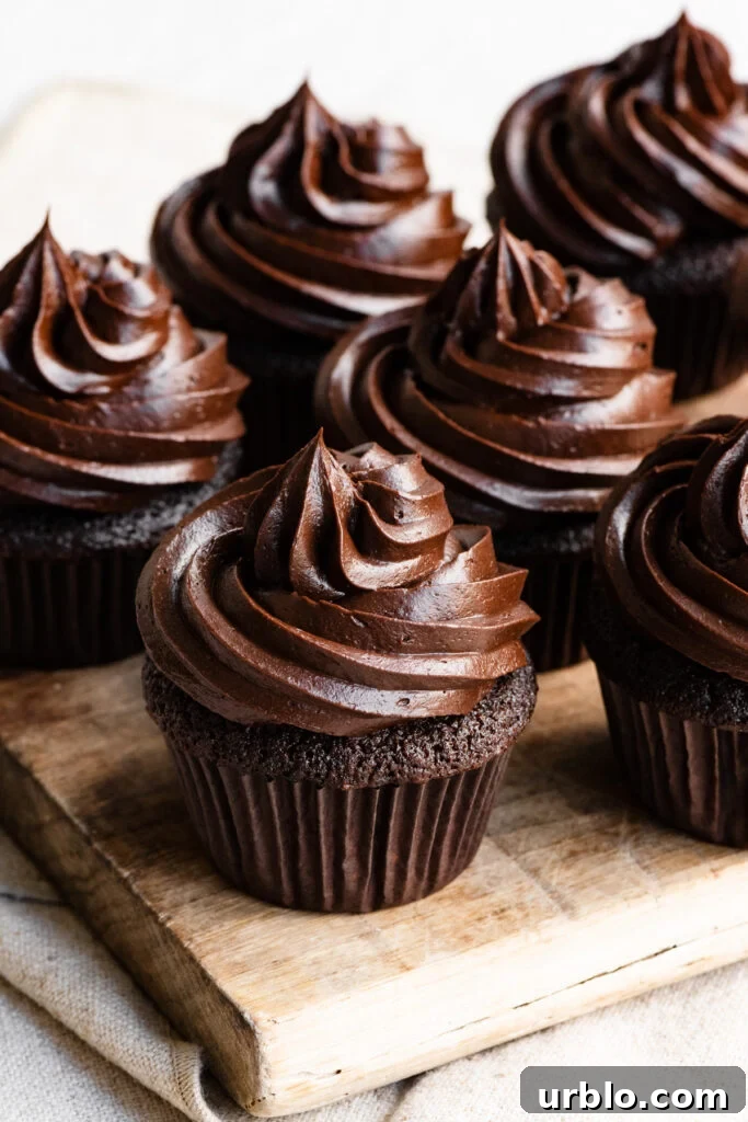 Silky Chocolate Ganache Buttercream Frosting Recipe 3 Five chocolate cupcakes topped with chocolate frosting on a wooden cuttingboard.