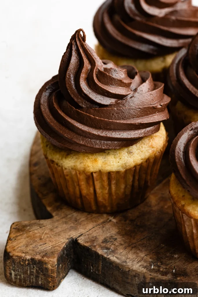 Silky Chocolate Ganache Buttercream Frosting Recipe 4 Close up of banana cupcakes topped with chocolate swirled frosting on a wooden cutting board.