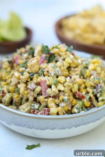 heaping bowl of mexican street corn dip with lime and chips in background