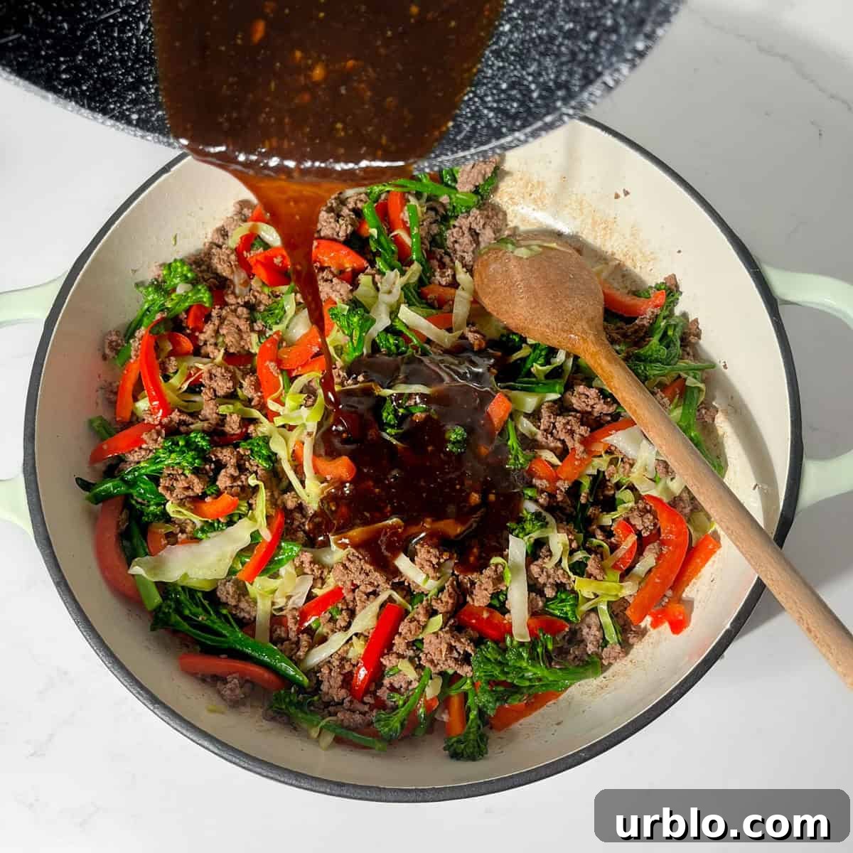 Adding the homemade teriyaki sauce to the meat and vegetables in a large frying pan.