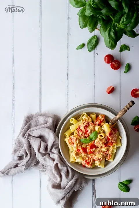 A bowl of tomato feta pasta surrounded by basil and chopped tomatoes