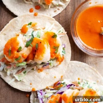 a close up view of bang bang shrimp tacos on a wooden board next to a bowl of bang bang sauce.