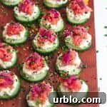 Smoked salmon cucumber bites topped with lemon zest and chives on a wooden board.
