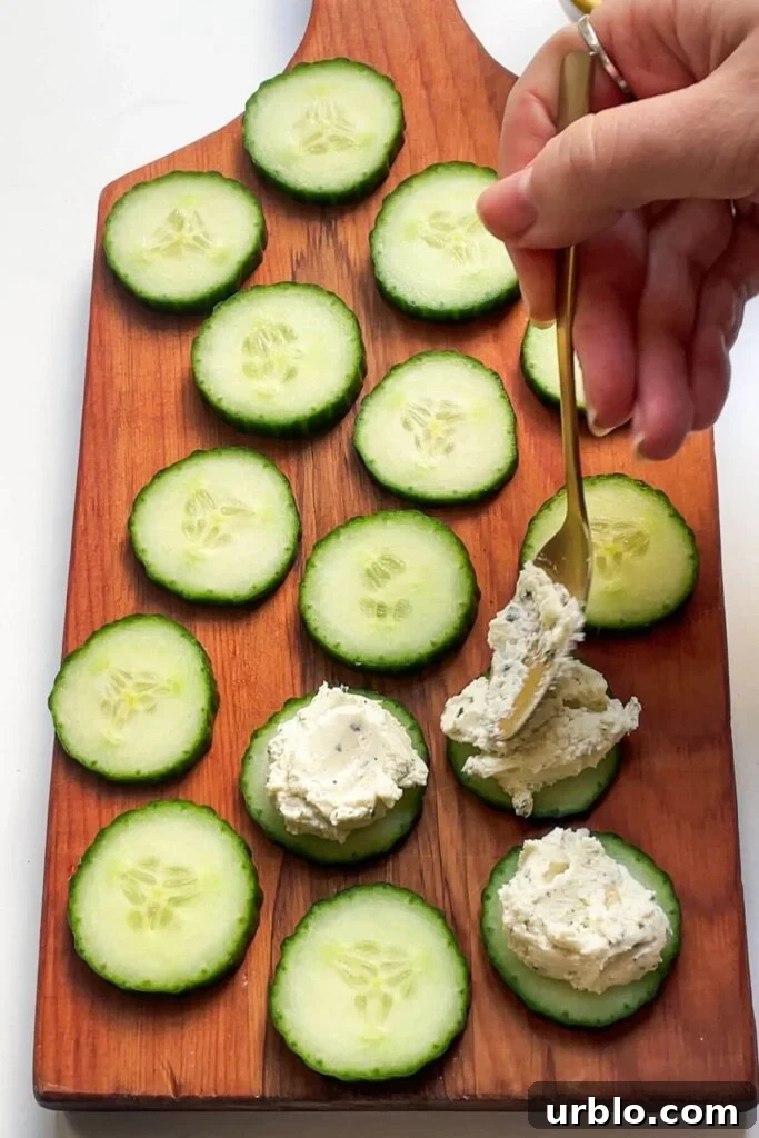 Spooning whipped boursin onto cucumber slices on a wooden board.