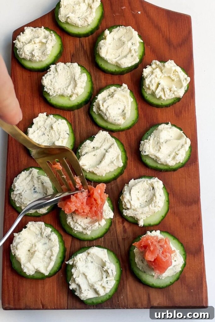 Spooning salmon on whipped boursin on a slice of cucumber.
