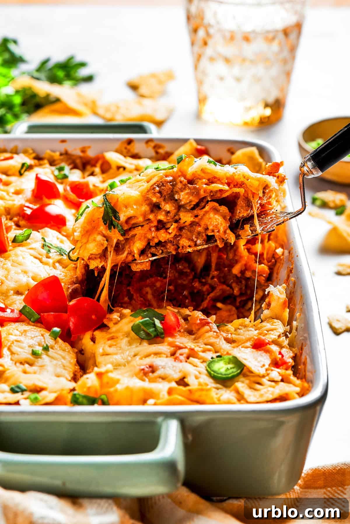 A serving spoon lifting out a slice of Dorito casserole from a baking dish.