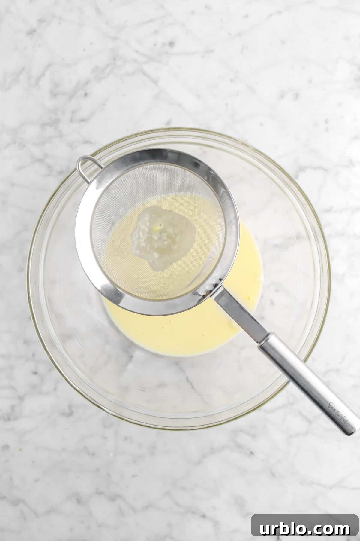 custard being strained through fine meshed sieve