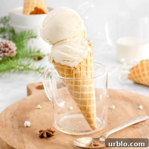 two scoops of ice cream in waffle cone in glass mug with spoon beside, upside down cone behind in stack of bowls, pine branch, and fairy lights