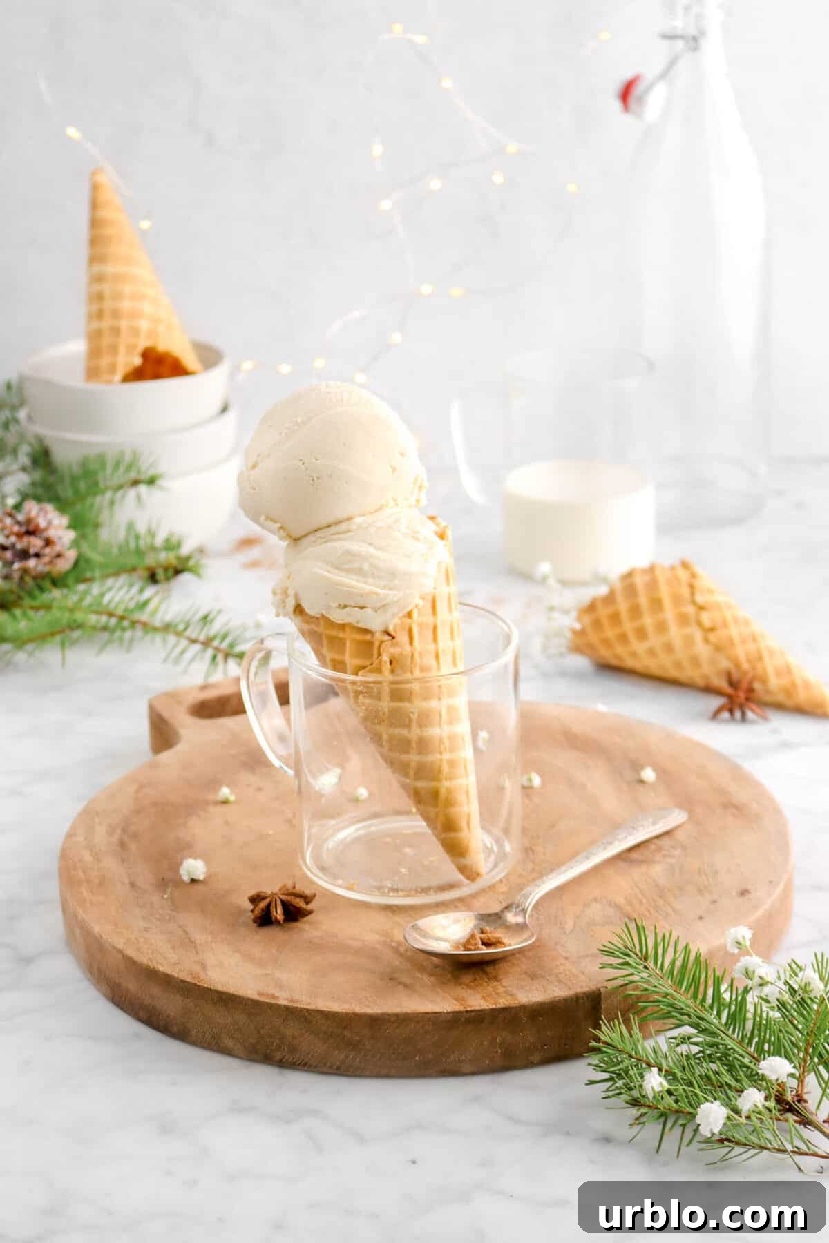 eggnog ice cream with pine branches around, flowers, mug of eggnog, and fairy lights behind