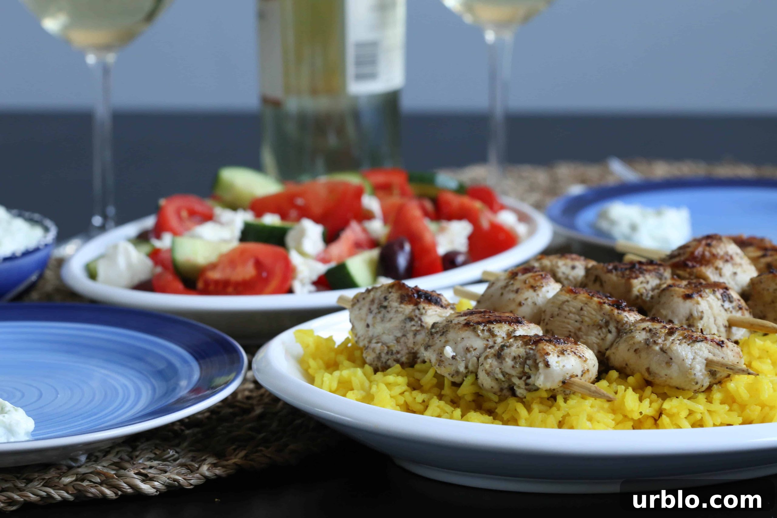 rice, chicken kabobs, and greek salad on a dinner table with plates and wine glasses.