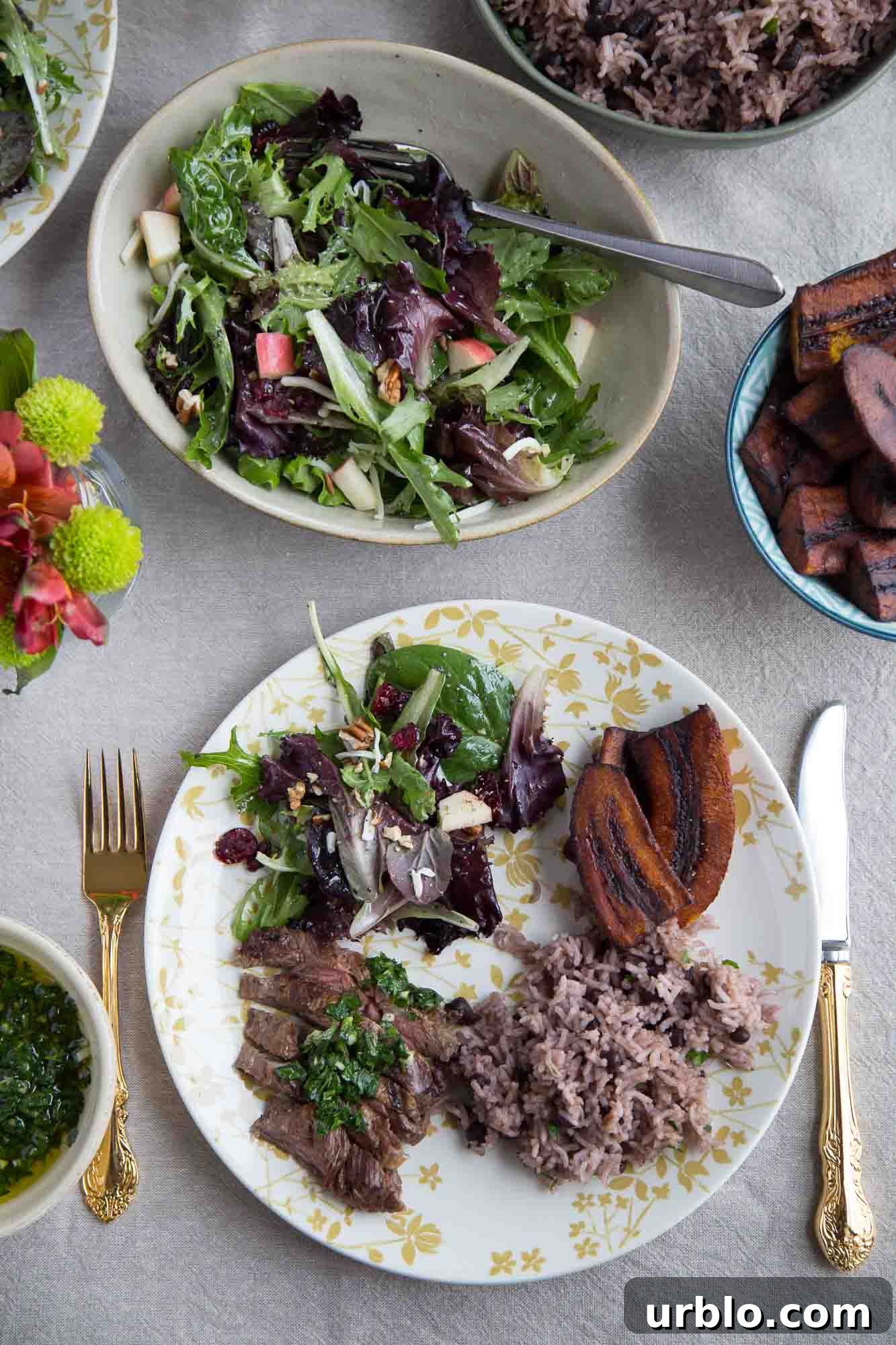 a dinner plate with steak, arroz moro, fried plantains, and salad on a dinner table.