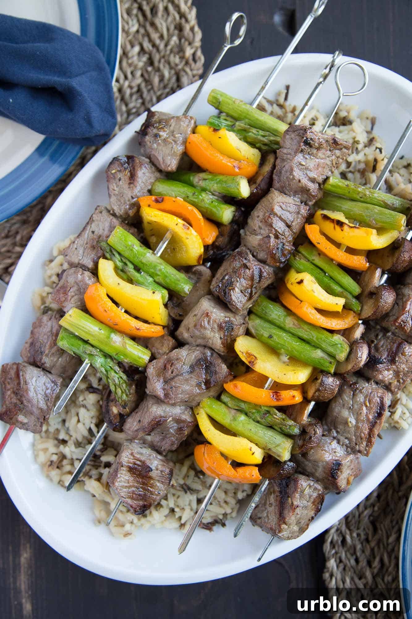 steak and veggie kabobs on top of wild rice, sitting on a white serving platter.