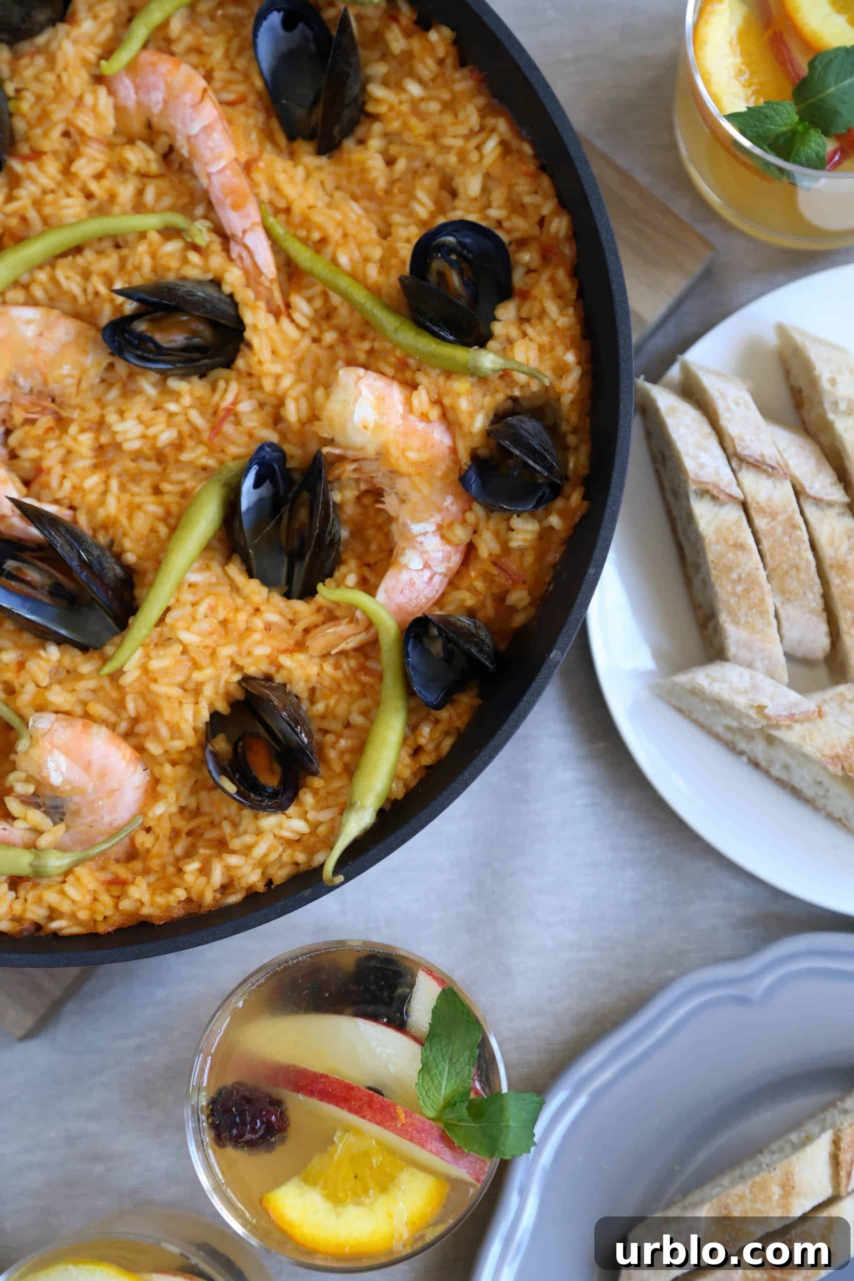 pan of seafood paella on a table with sliced bread and a glass of sangria.