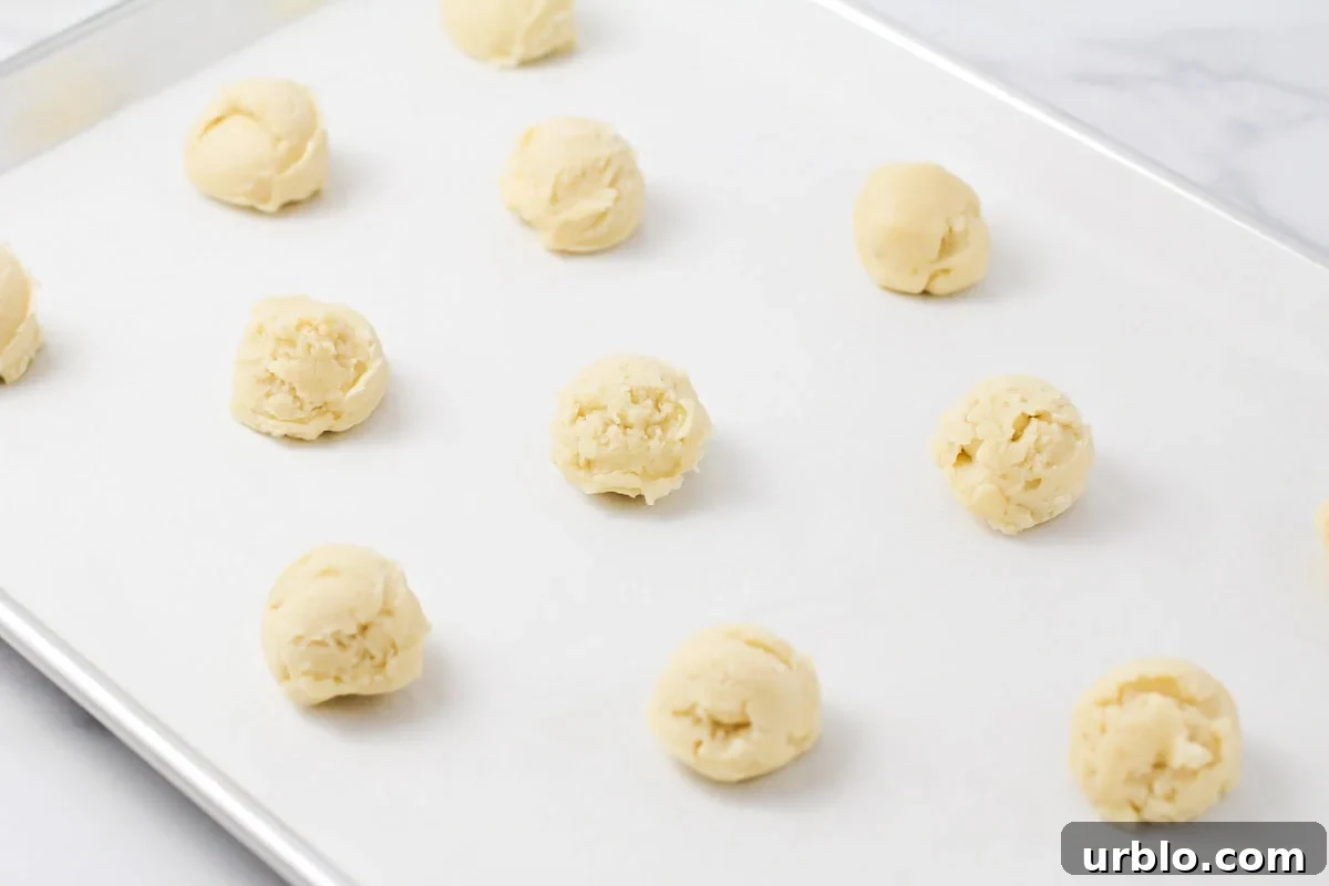 Dropped cookie dough balls on a lined baking sheet.