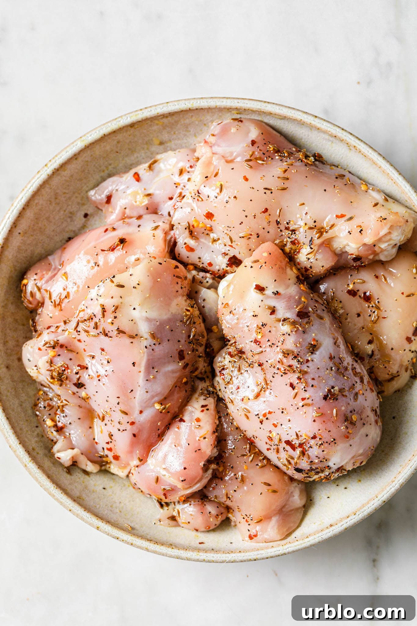 Uncooked bone-in skinless chicken thighs in a bowl.