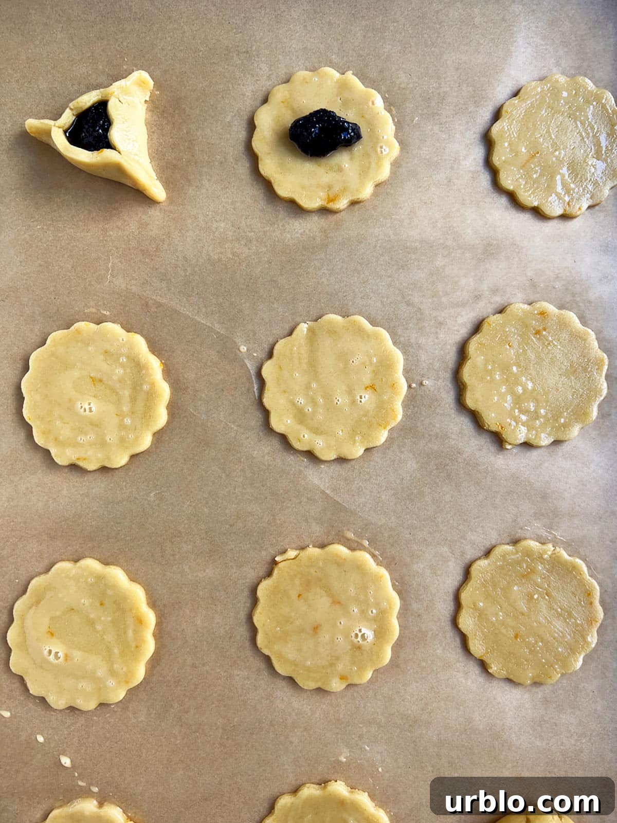 Unbaked hamantaschen on parchment with poppy seed filling in two of them.