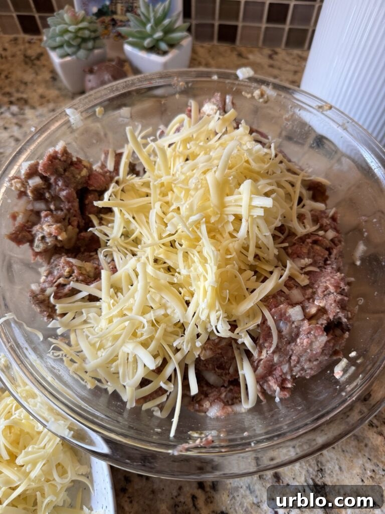 Grated cheese on top of a ground beef mixture in a glass bowl.