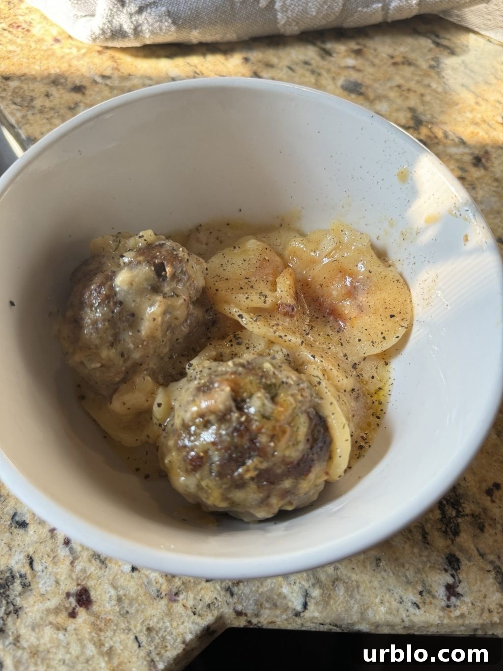A bowl of two Au Gratin meatballs.
