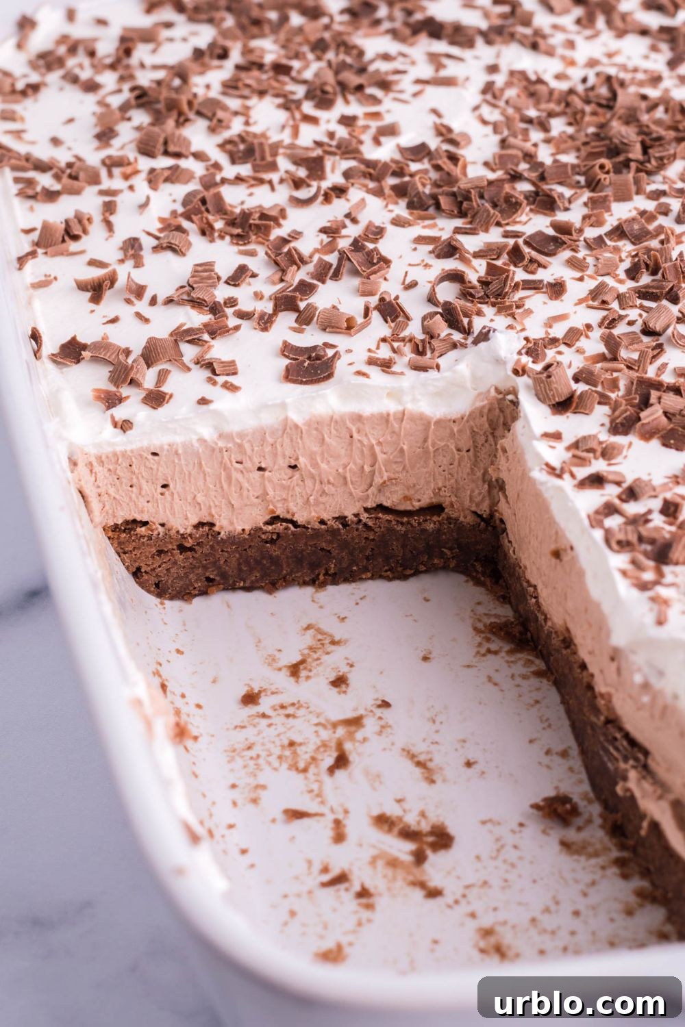 layered brownie dessert in pan with some pieces cut out to showcase the layers