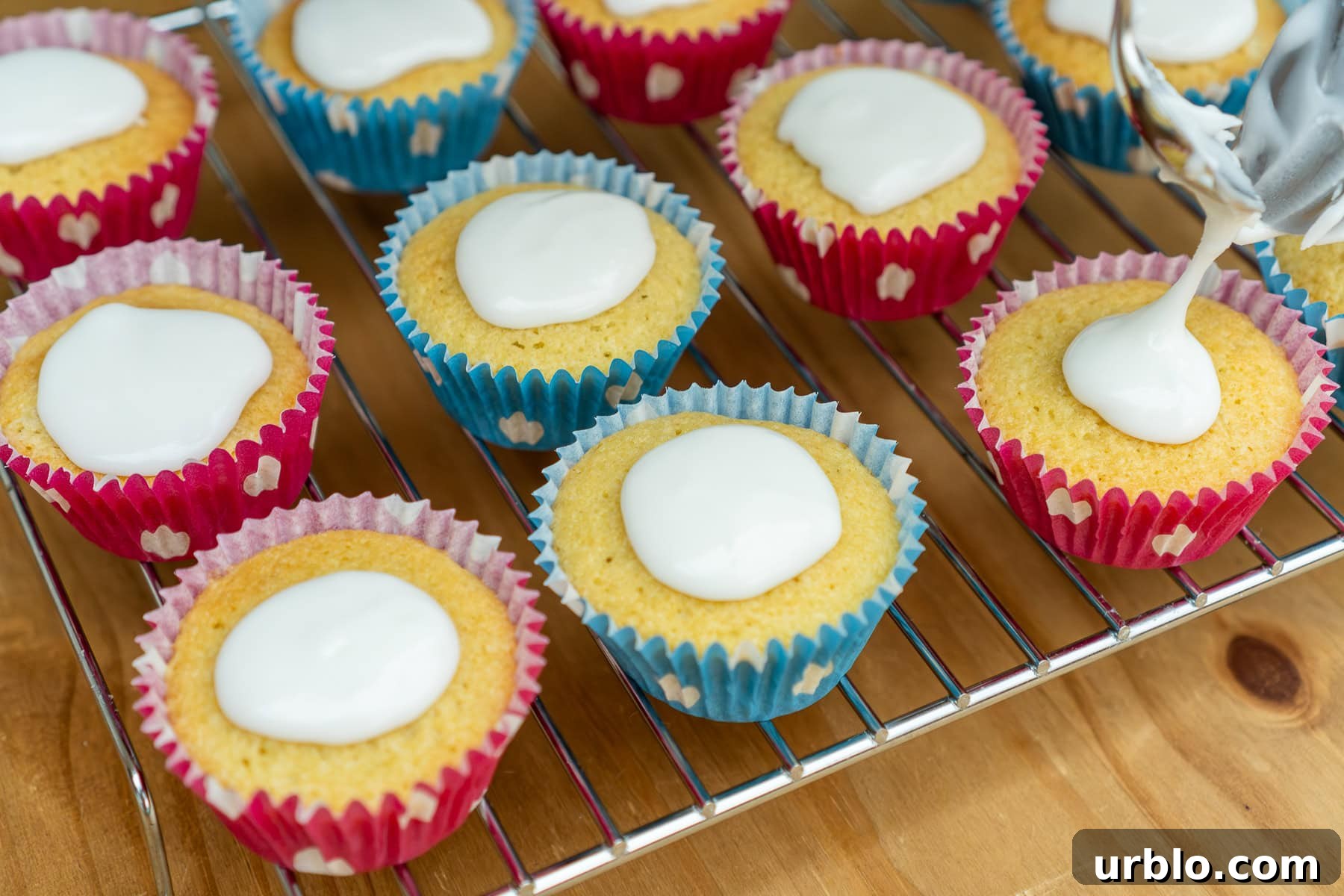 Fairy cakes on a wire rack with icing being put on top of each cake