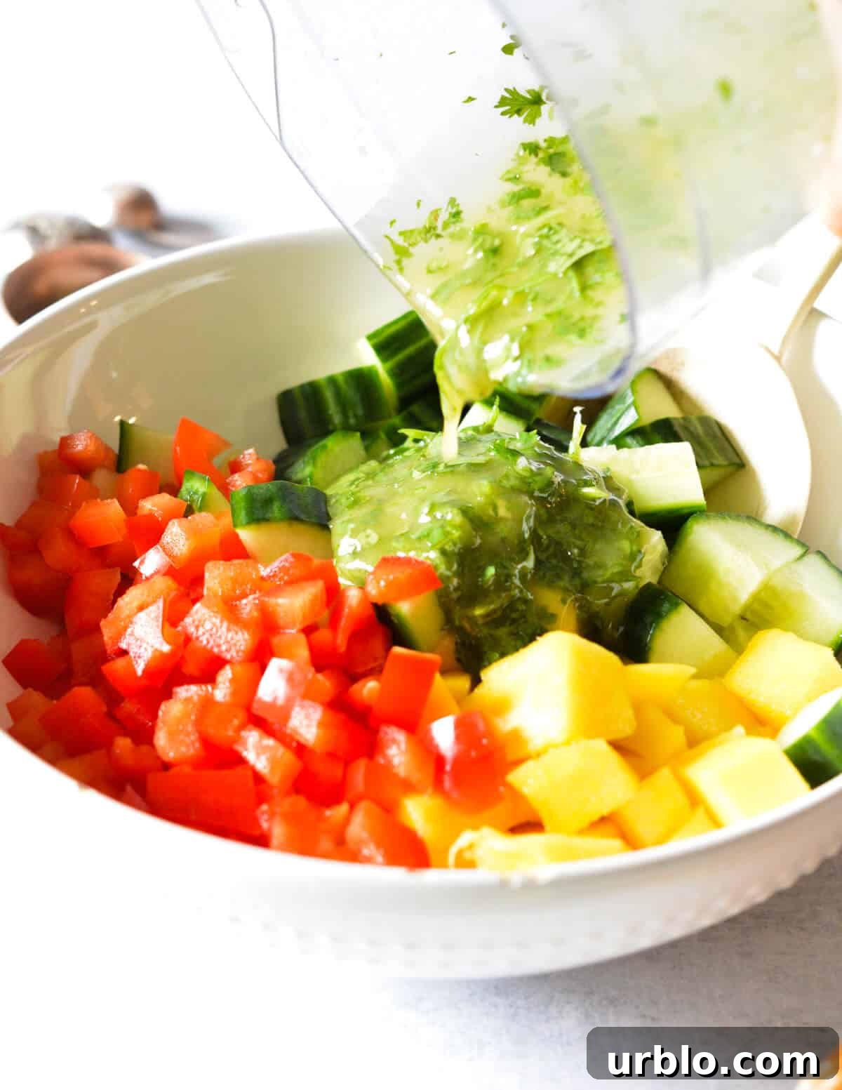 pouring cilantro vinaigrette over mango, cucumber, and bell peppers.